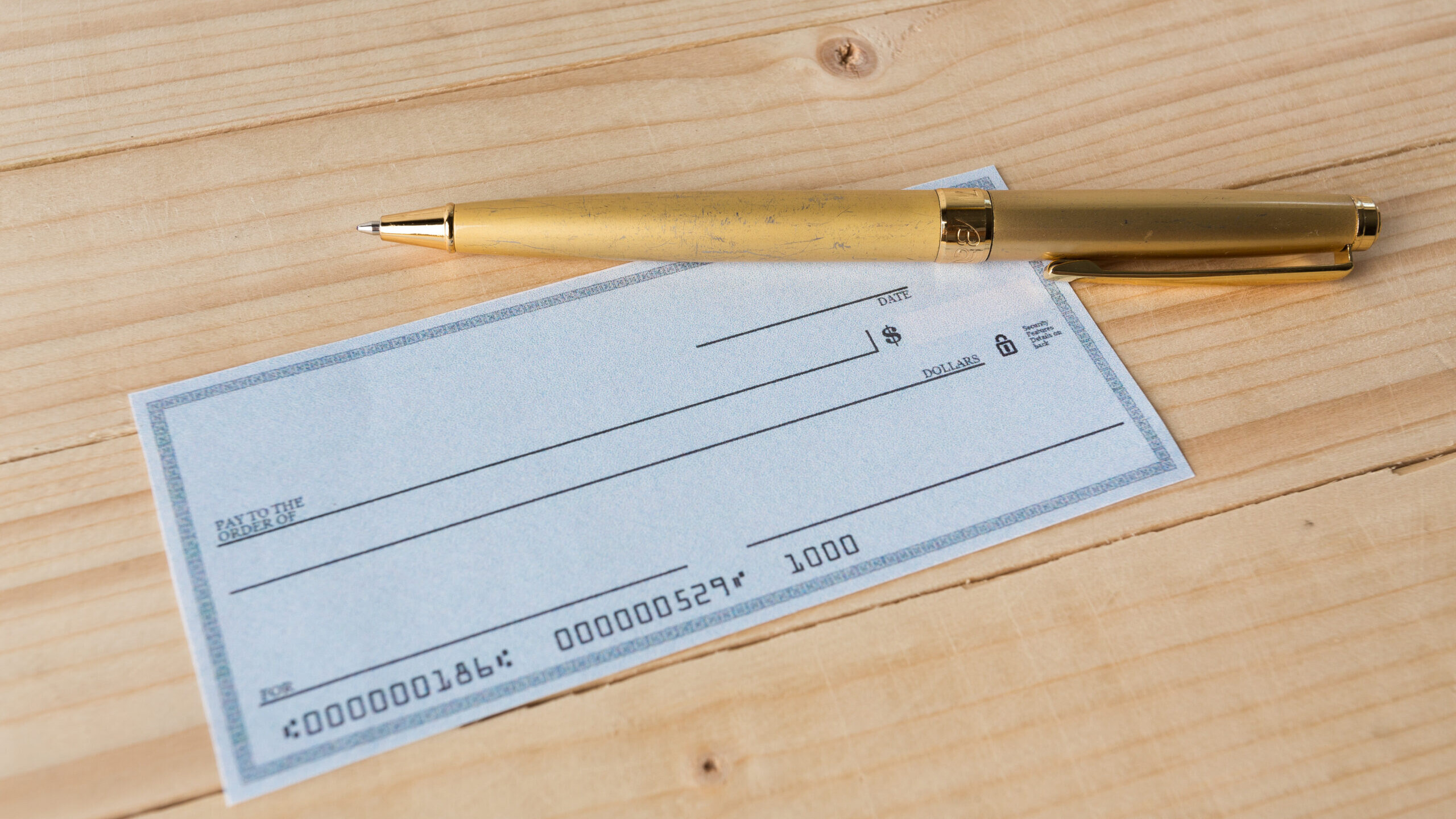 blank check with gold pen on wood table