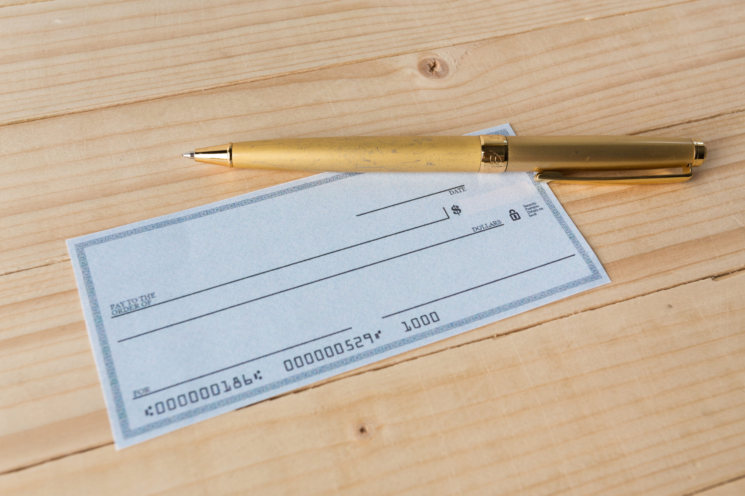 blank check with gold pen on wood table