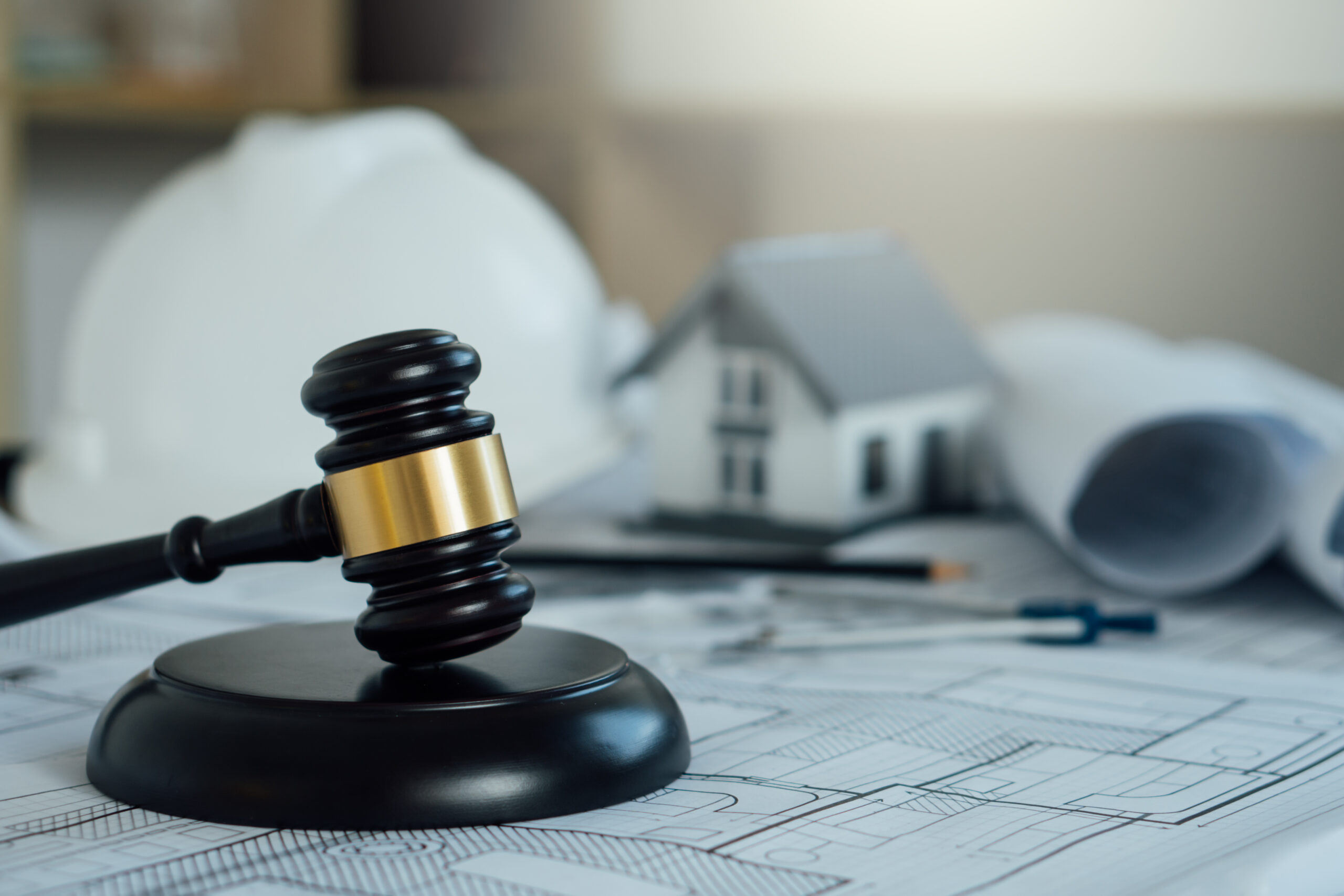 Gavel on architectural blueprints with a hard hat and model house in the background, representing real estate law and regulations.